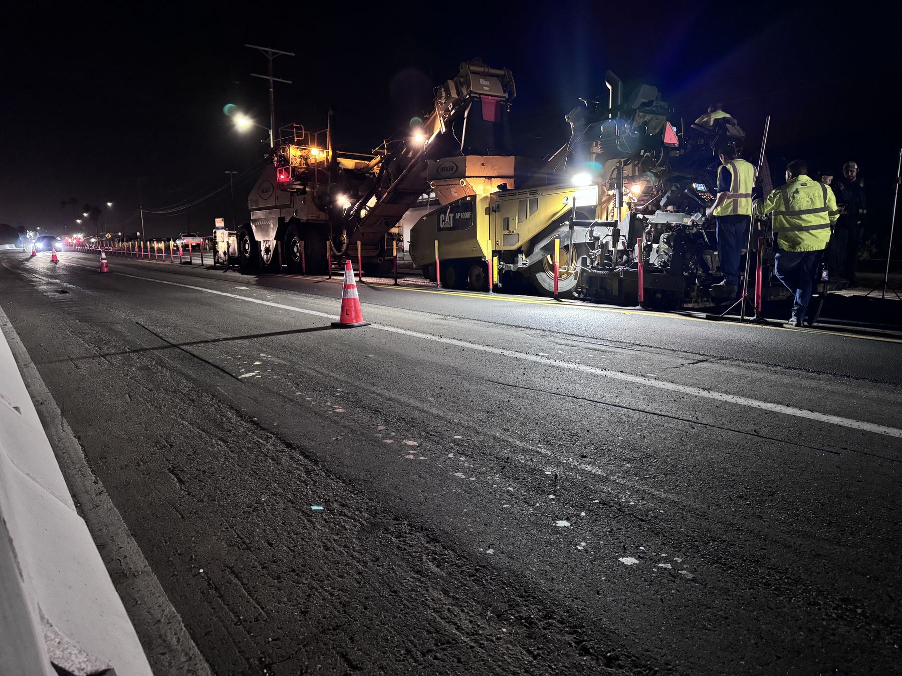 Night highway paving train laying hot mix under lights